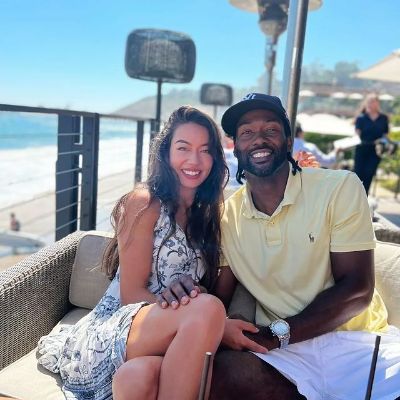 Both are sitting and posing while holding hands.